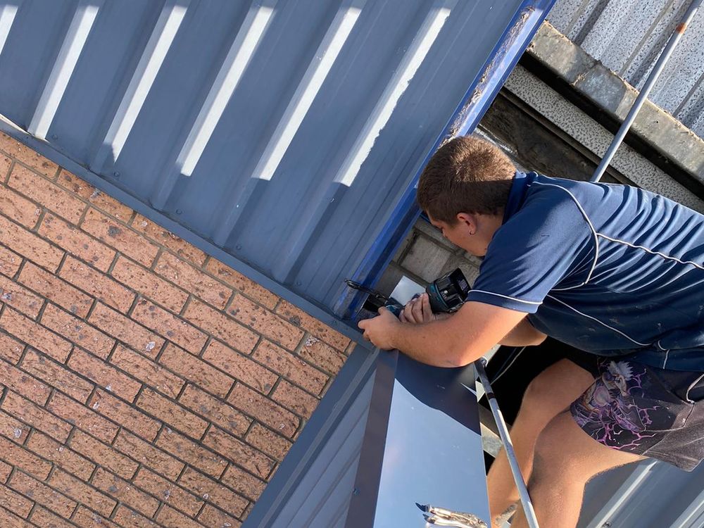 ADKO roofer fixing flashing where a metal roof meets a brick wall