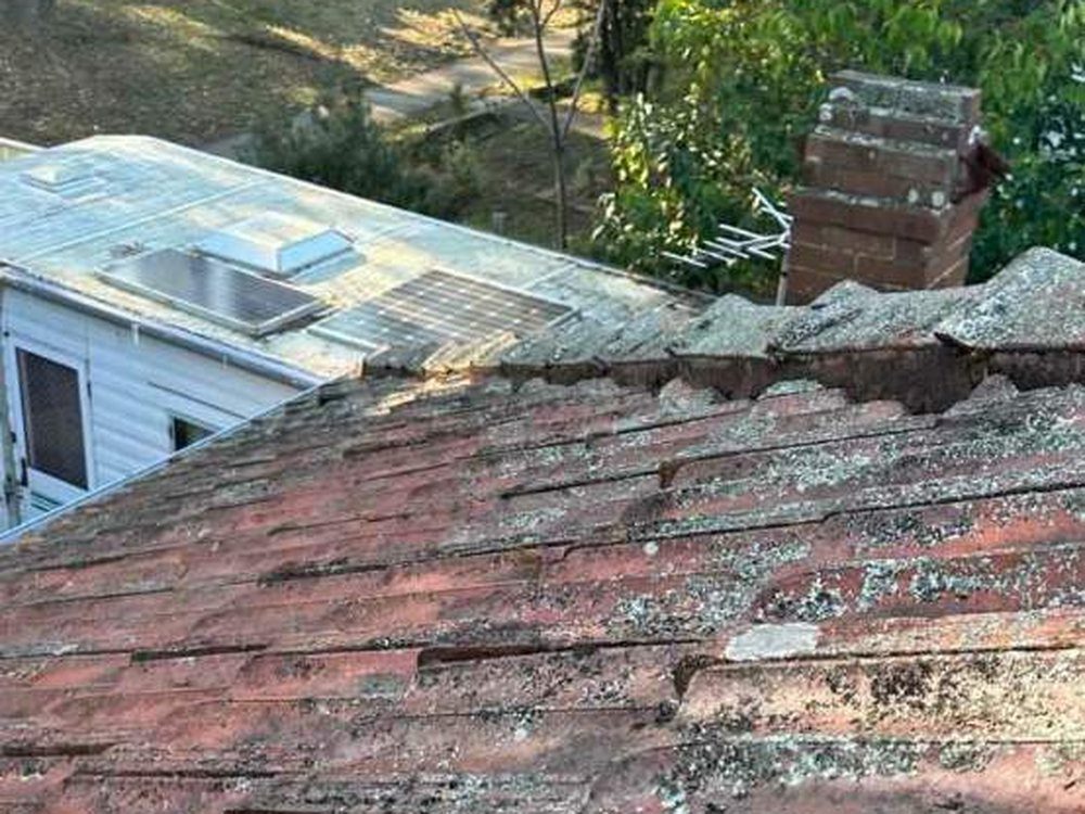 Weathered tile roof covered in moss and lichen before a restoration